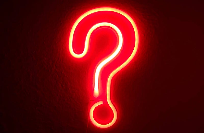 A neon red question mark sign on a dark wall.