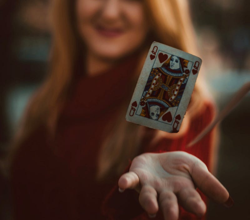 A smiling woman holds a Queen of Heart’s playing card.