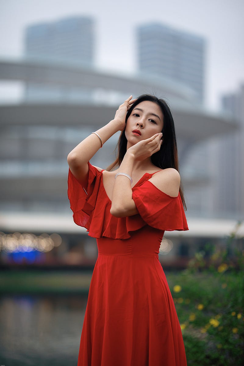 A Chinese woman in a red dress holds her face and looks at the camera.