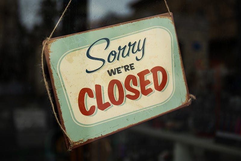 A sorry we’re closed sign hangs in a shop window.